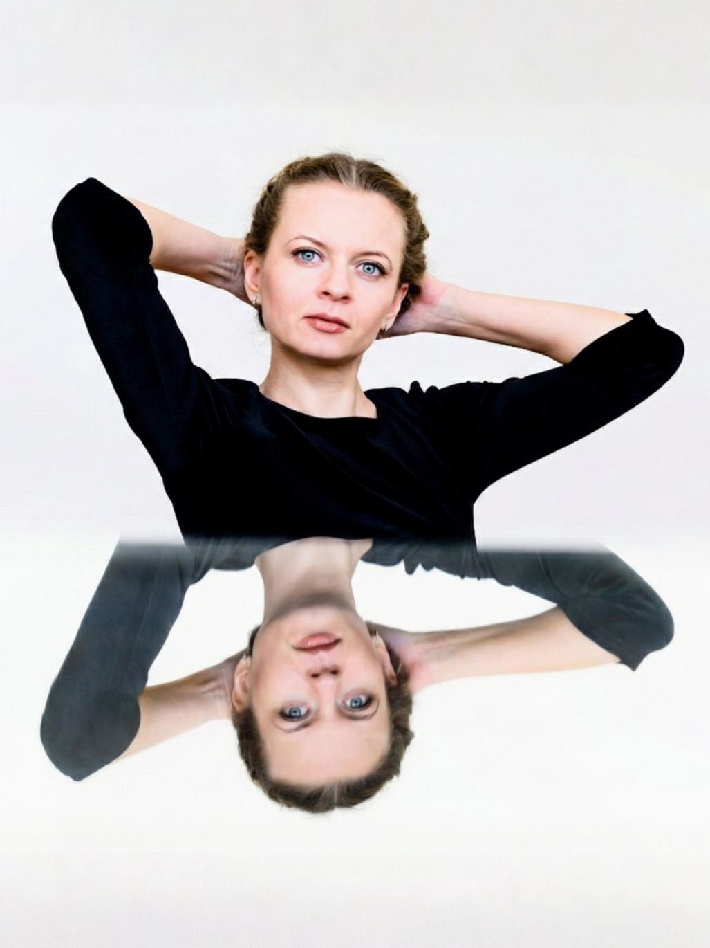 Ritratto in studio in nero, riflesso su una superficie a specchio su fondo bianco.